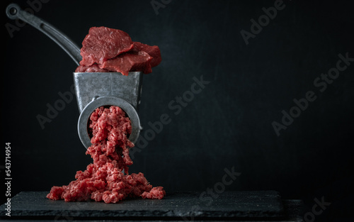Making minced meat for beef meatballs in a manual meat grinder on a black background. Macro shot. Close up of metal meat grinder with raw meat photo