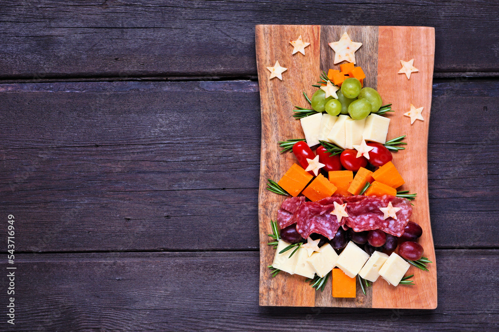 Christmas tree charcuterie board. Top view over a dark wood background. Selection of cheese and meat appetizers.