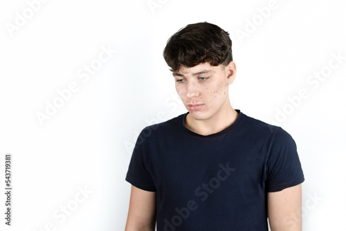 Portrait of a sad teenager boy on a light background, he looks to the side and down, the boy has problems with the skin of his face, many pimples and blackheads © Мар'ян Філь
