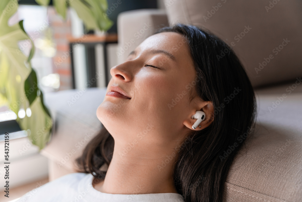 Close up of calm young woman in wireless headphones relaxing on sofa