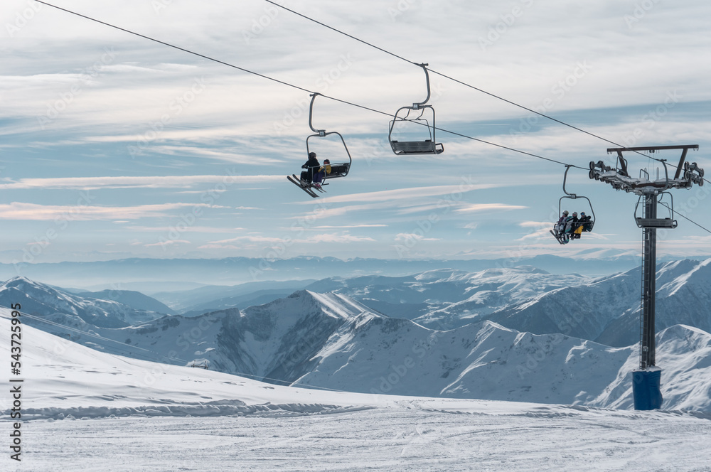 skiers and snowboarders on ski lift at winter at resort