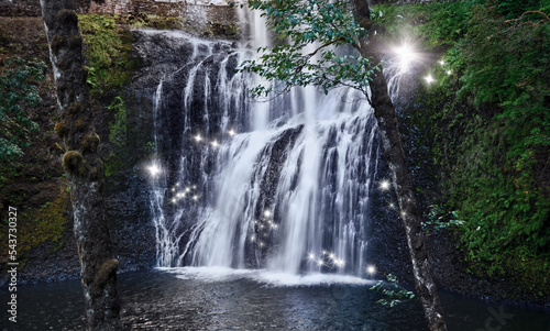 Waterfall with fairy sparks of shimmering light in magical forest