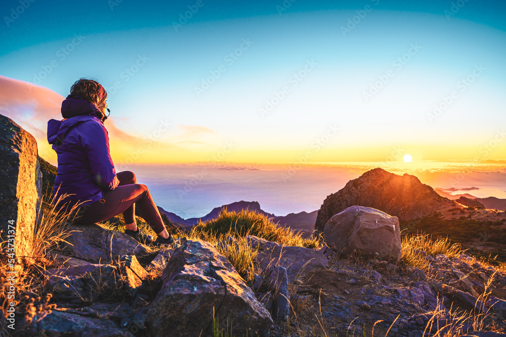 Naklejka premium Sitting woman watching the sunrise over the beautiful mountain landscape of Pico do Ariero. Pico do Arieiro, Madeira Island, Portugal, Europe.