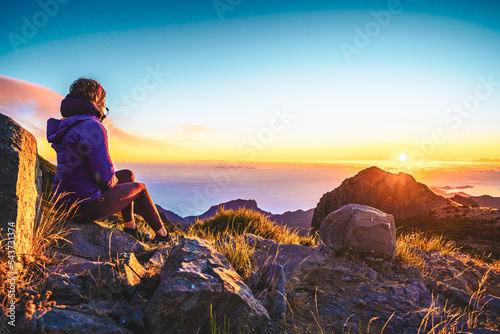 Sitting woman watching the sunrise over the beautiful mountain landscape of Pico do Ariero. Pico do Arieiro, Madeira Island, Portugal, Europe.