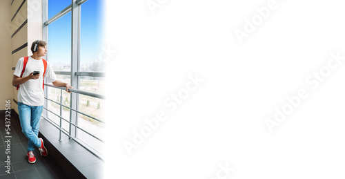 Guy student in headphones stands and looks out the big window. Selective focus, banner