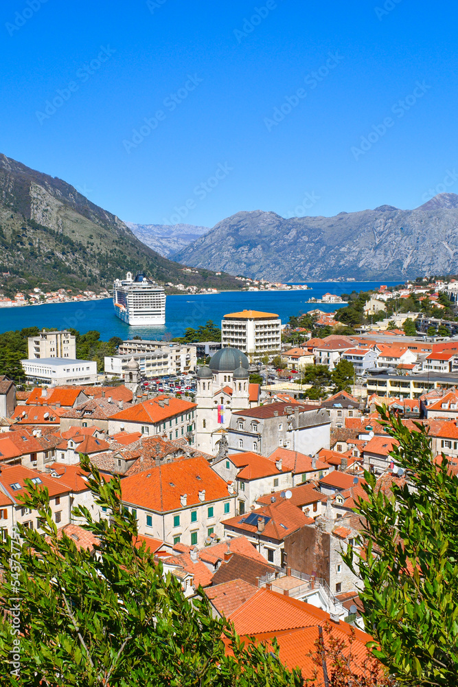 Kotor, Montenegro, Europe. Bay of Kotor on Adriatic Sea. Roofs of the historical buildings in the old town, sea and mountains in the background. Clear blue sky, sunny day.