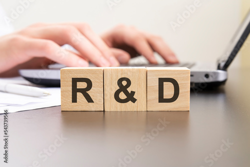 r and d - acronym from wooden blocks with letters. background hands on a laptop with blur. business concept.