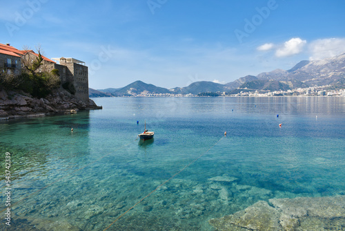 Small fishing boat on the Adriatic sea near Sveti Stefan Island, Montenegro. Turquiose water, islet with historical buildings. Mountains in the background. Fishing concept.