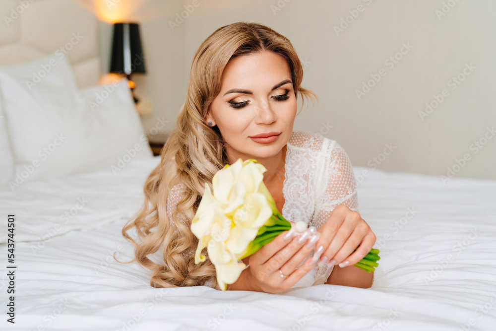 beautiful blonde in a white peignoir with a bouquet of flowers lying in bed.