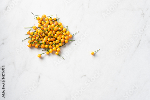 A bright yelllow aji charapita pepper sits apart from a pile on a white marble surface photo