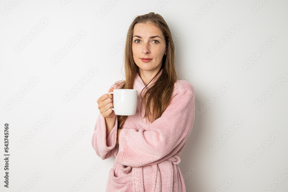 Sad young woman in a bathrobe drinks coffee on a white background Sad young woman in a bathrobe drinks coffee on a white background