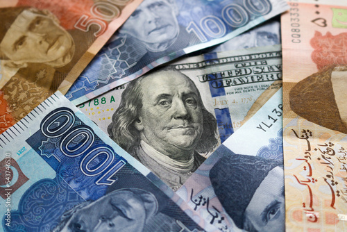 Closeup of hundred US American paper banknote currency under pakistani rupee. Concept of loan. 
