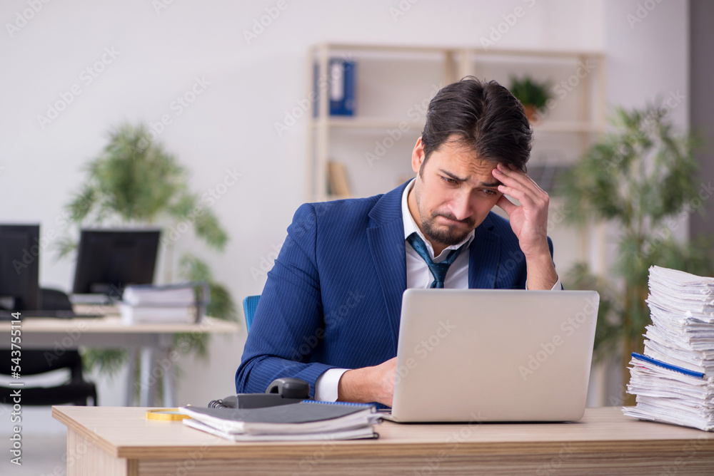 Young male employee unhappy with excessive work in the office Young male employee unhappy with excessive work in the office
