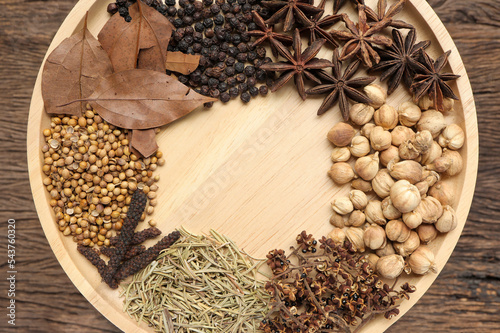 Various herbs and spices for cooking in wooden plate on a wooden background. Top view.