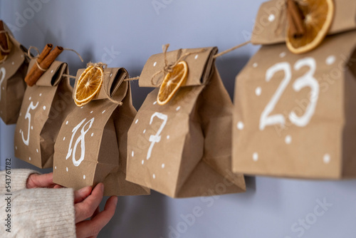 Advent calendar from craft paper with dry oranges and cinnamon on the wall with woman's hands.