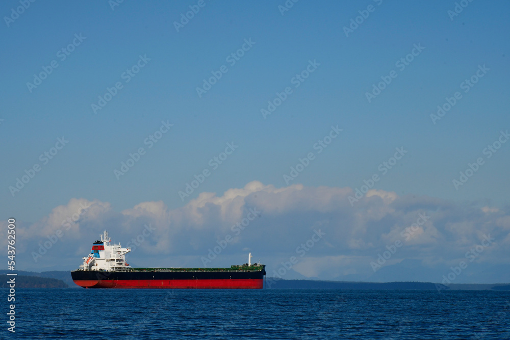 A large red and black cargo ship in mid harbor waiting to off load its cargo. 