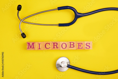 Word Microbes made with wooden cubes and stethoscope on yellow background  top view