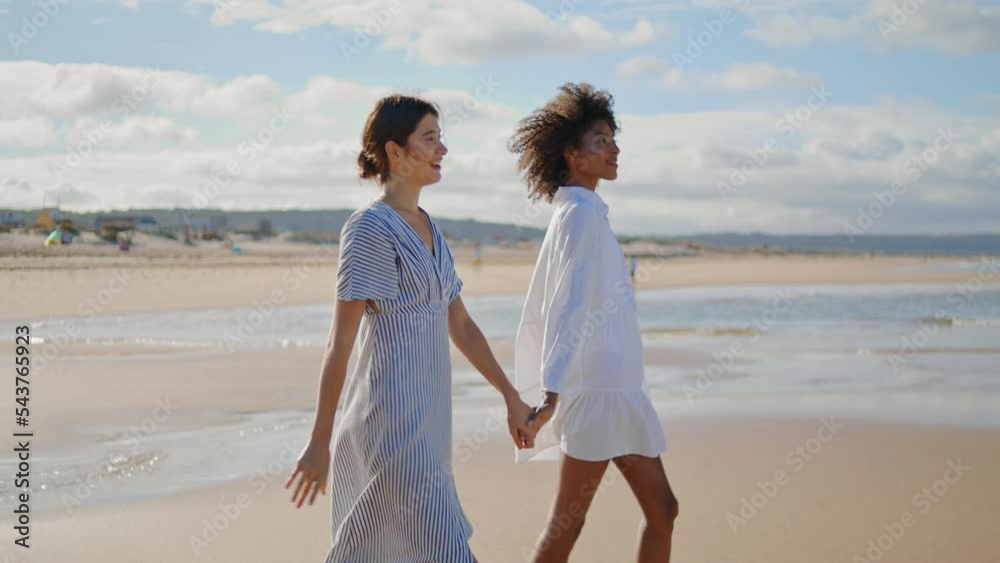 Joyful lesbian couple walking sea shore on sunny day. Happy girls holding hands Joyful lesbian couple walking sea shore on sunny day. Happy girls holding hands