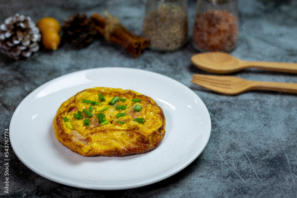 Breakfast yellow omelette with bacon topped with sliced spring onions on dark concrete close up view.