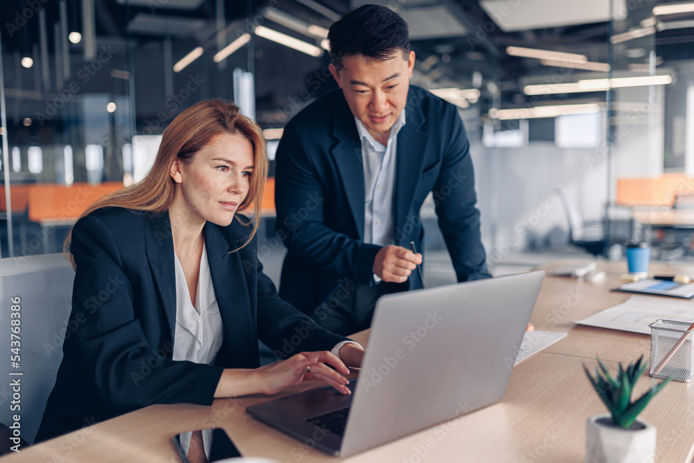 Two multiethnic coworkers working together analyzing the charts in office Two multiethnic coworkers working together analyzing the charts in office