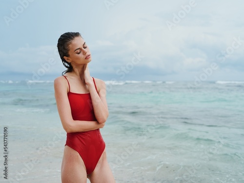 Sexy woman in red swimsuit on the ocean beach with wet hair does yoga  slim pumped body sunscreen