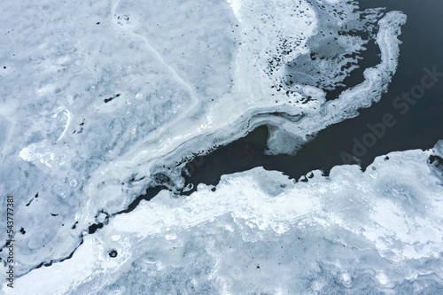 aerial drone view of frozen lake with blue ice on dark water surface. drone photo. © Mr Twister