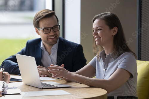 Happy positive businesspeople, business partners working together seated at desk in modern office room, discuss fresh creative ideas, consider common task, have fun, joking engaged in group meeting