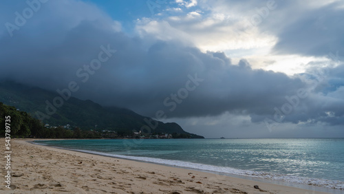 A calm foggy day on a tropical beach. The foam of the waves of the turquoise ocean on the sand. The top of the hill is hidden in clouds. Seychelles. Mahe. Beau Vallon