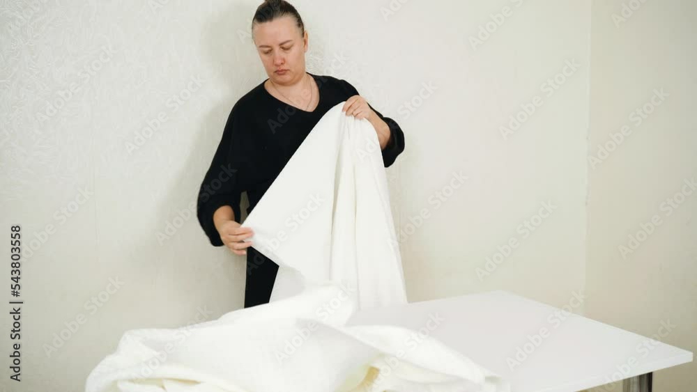 Work at home. Small business. A female seamstress measures a white fabric on a table. Work at home. Small business. A female seamstress measures a white fabric on a table.