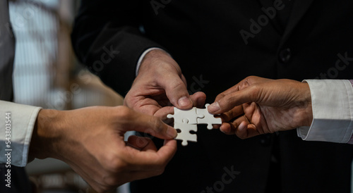 Businessmen join puzzle pieces in office, concept of teamwork and partnership, colleagues hold jigsaws coordinated.