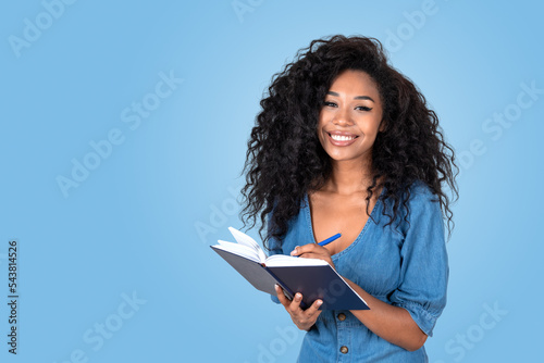 Young black woman taking notes and smiling, copy space blue background
