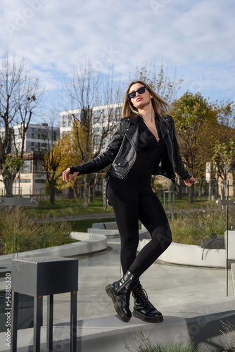 Fashionable young woman with long hair wearing solid long sleeve bodycon one piece jumpsuits posing in a black leather jacket and smooth platform boots photo