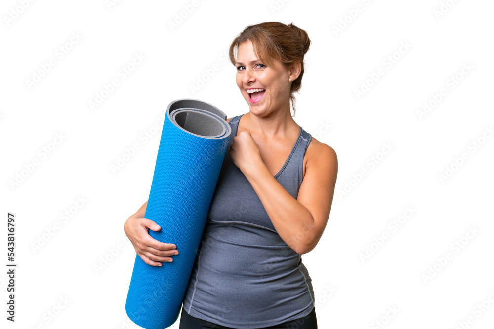 Middle-aged sport woman going to yoga classes while holding a mat over isolated background celebrating a victory Middle-aged sport woman going to yoga classes while holding a mat over isolated background celebrating a victory