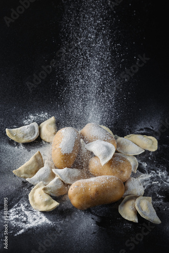 Dumplings, mushrooms and potatoes on a black background are covered with flour