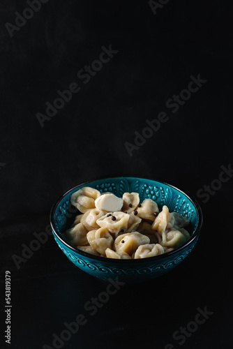 top view on ready russian pelmeni with meat fillin served with fresh salad leaves in deep gray bowl on black background photo