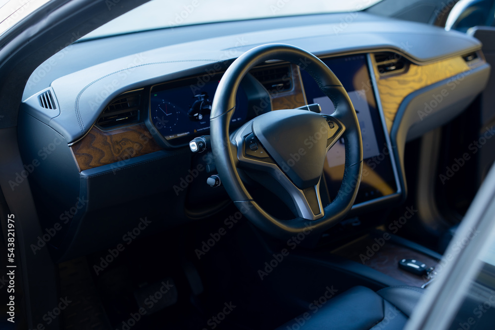 Inside car interior with front seats, textile, windows, door, console. Electric car interior details. Modern and futuristic SUV electric car with vertical door and large touch screen dashboard, wheel