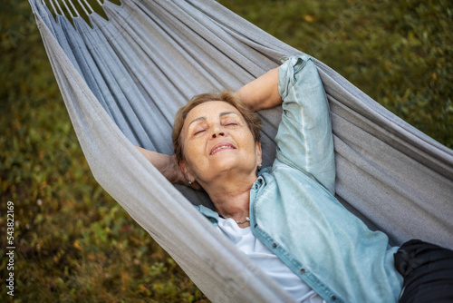 Beautiful happy elderly woman relaxing in a hammock in the garden of a country house. Happy retirement lifestyle