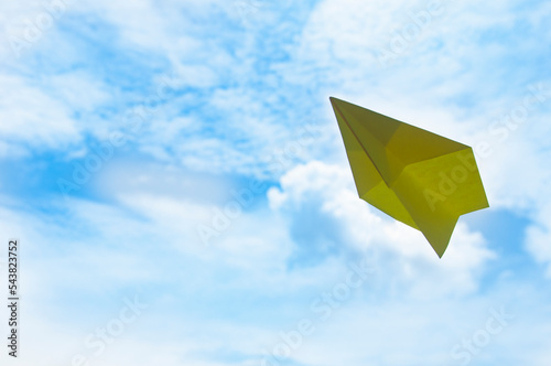 Flying yellow paper plane on blue sky background. Travelling concept.