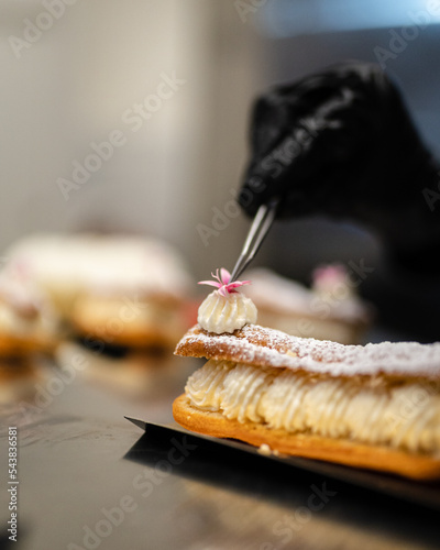 Une pâtissière dépose une fleur avec des pincettes sur un gâteau 