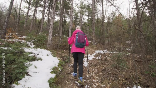 Girl hiking in nature during winter time. Back view of backpacker walking on a path in the forest with snow.