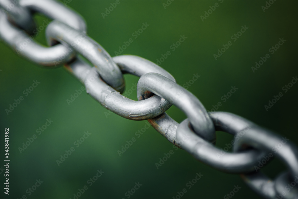 Closeup to a stainless shiny chain links against green backdrop Closeup to a stainless shiny chain links against green backdrop