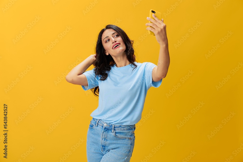 Woman blogger with a phone in her hands in a blue t-shirt and jeans on a yellow background smile signs gestures symbols, online communication and video call, copy space, free background Woman blogger with a phone in her hands in a blue t-shirt and jeans on a yellow background smile signs gestures symbols, online communication and video call, copy space, free background