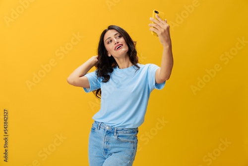 Woman blogger with a phone in her hands in a blue t-shirt and jeans on a yellow background smile signs gestures symbols, online communication and video call, copy space, free background