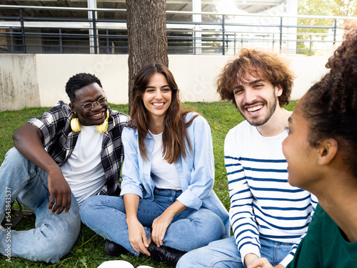 Group of young diverse friends sitting happily on the grass in a park or on campus. University students having a good time photo