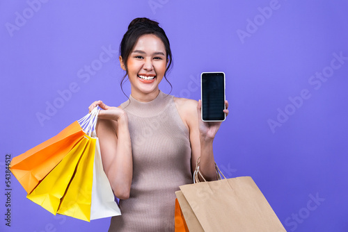 Asian young beautiful women are using smart phone shopping online with a shopping bag isolated in violet color background with copy space.