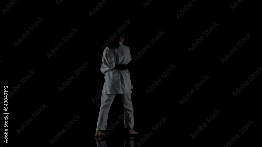 Young girl wearing kimono and practicing karate against black background Young girl wearing kimono and practicing karate against black background