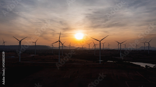 Aerial view of powerful wind turbine farm for pure energy production on beautiful sunset sun setting behind wind turbine producing alternative energy for sustainable development. renewable energy