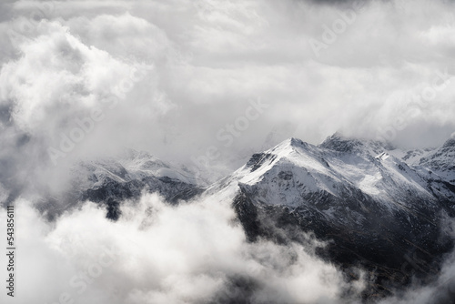 A landscape of the Dolomites Mountain Range covered in the fog under a cloudy sky in Italy.