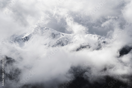 A landscape of the Dolomites Mountain Range covered in the fog under a cloudy sky in Italy.