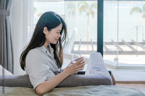 Asian woman holding a glass of water and sitting on sofa